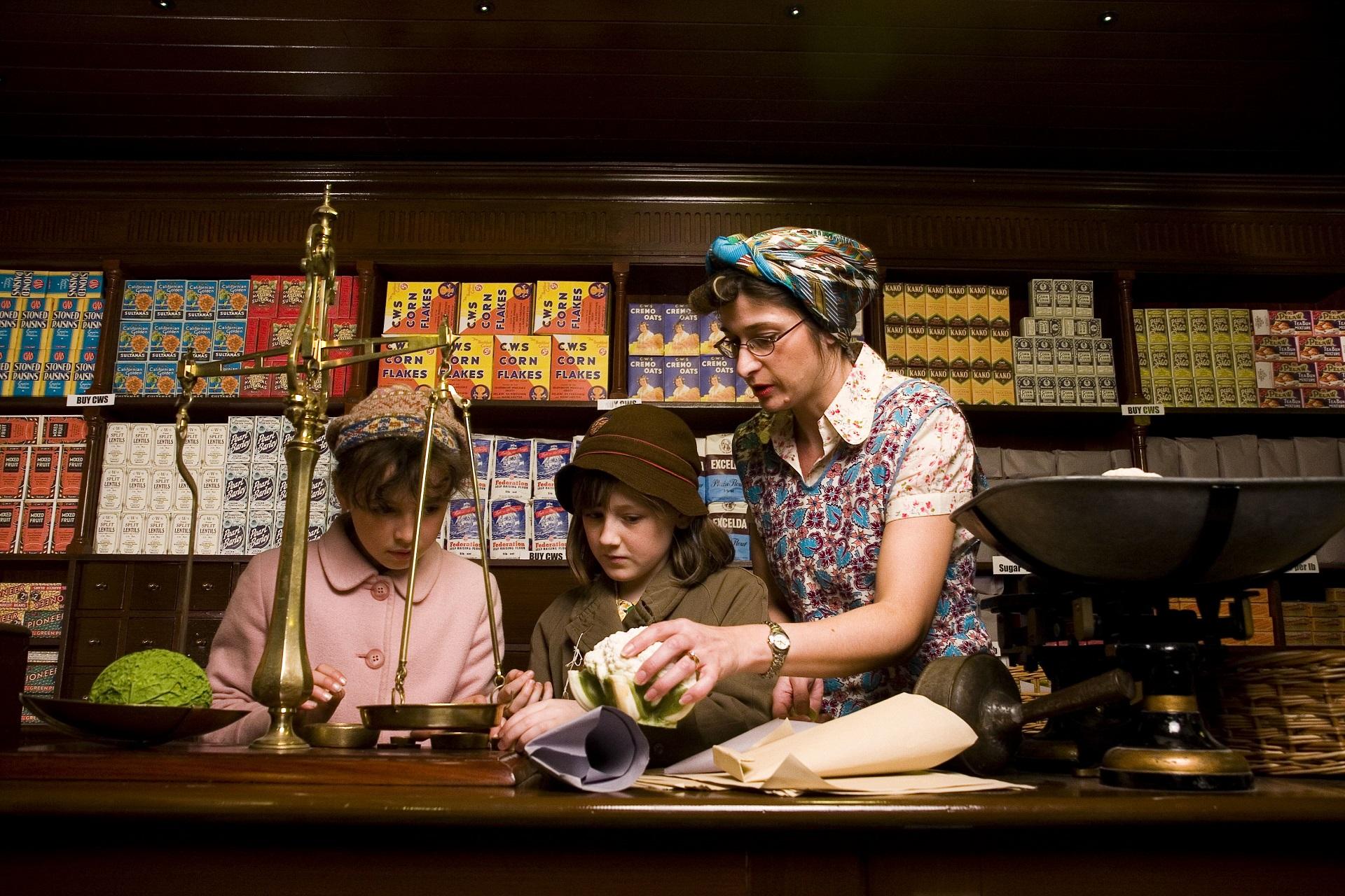 Two children and a woman dressed in 1940s clothing in a grocery shop.