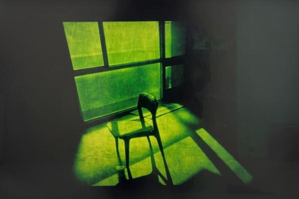 Light shines through a window. It casts shadow on a chair. There is a green cast to the image.