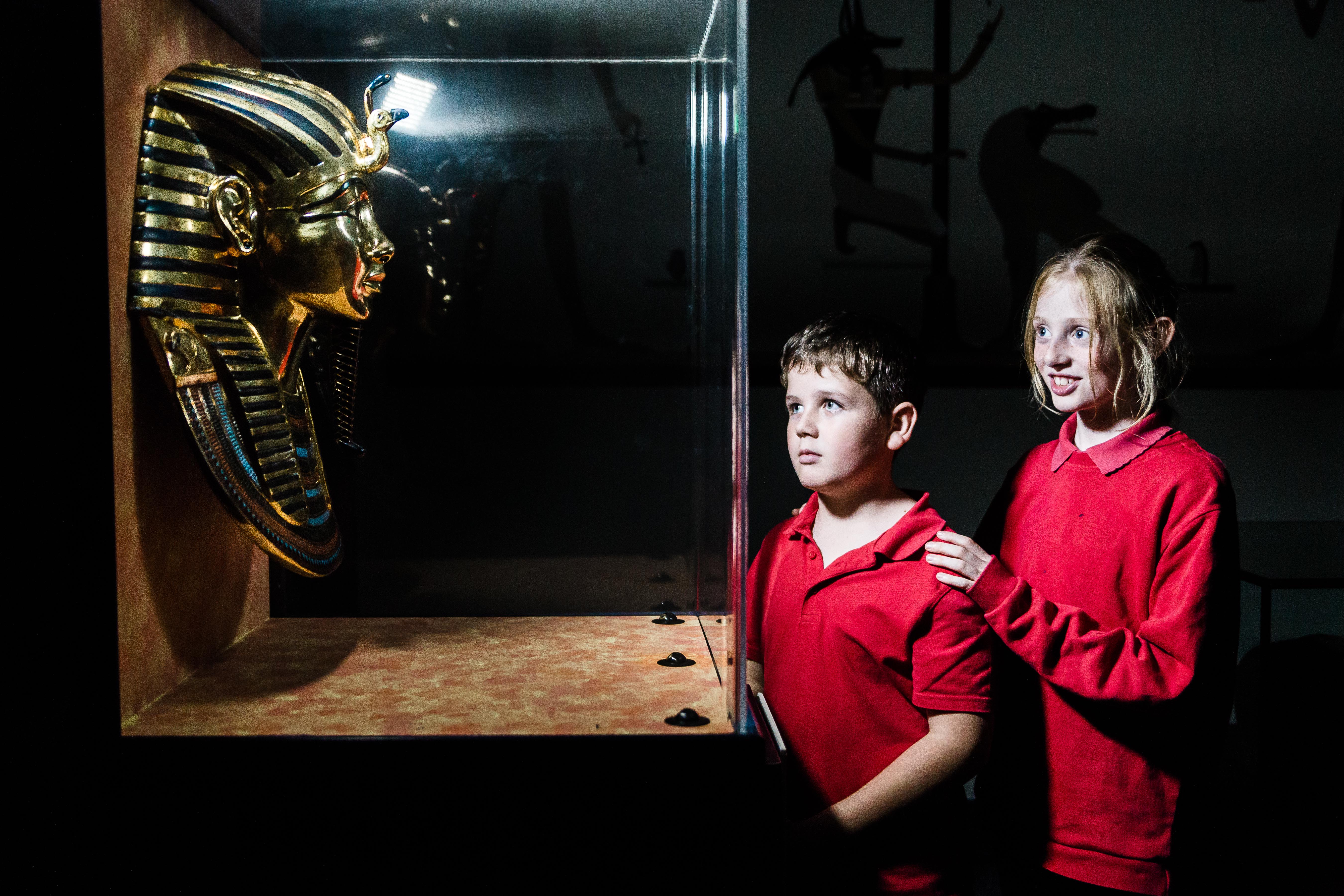 Two children are stood looking at the golden death mask replica of Tutankhamun.
