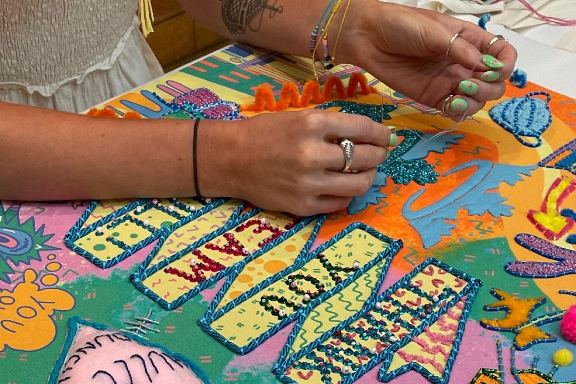 The pair of hands of an artist working on an embroidered piece of artwork