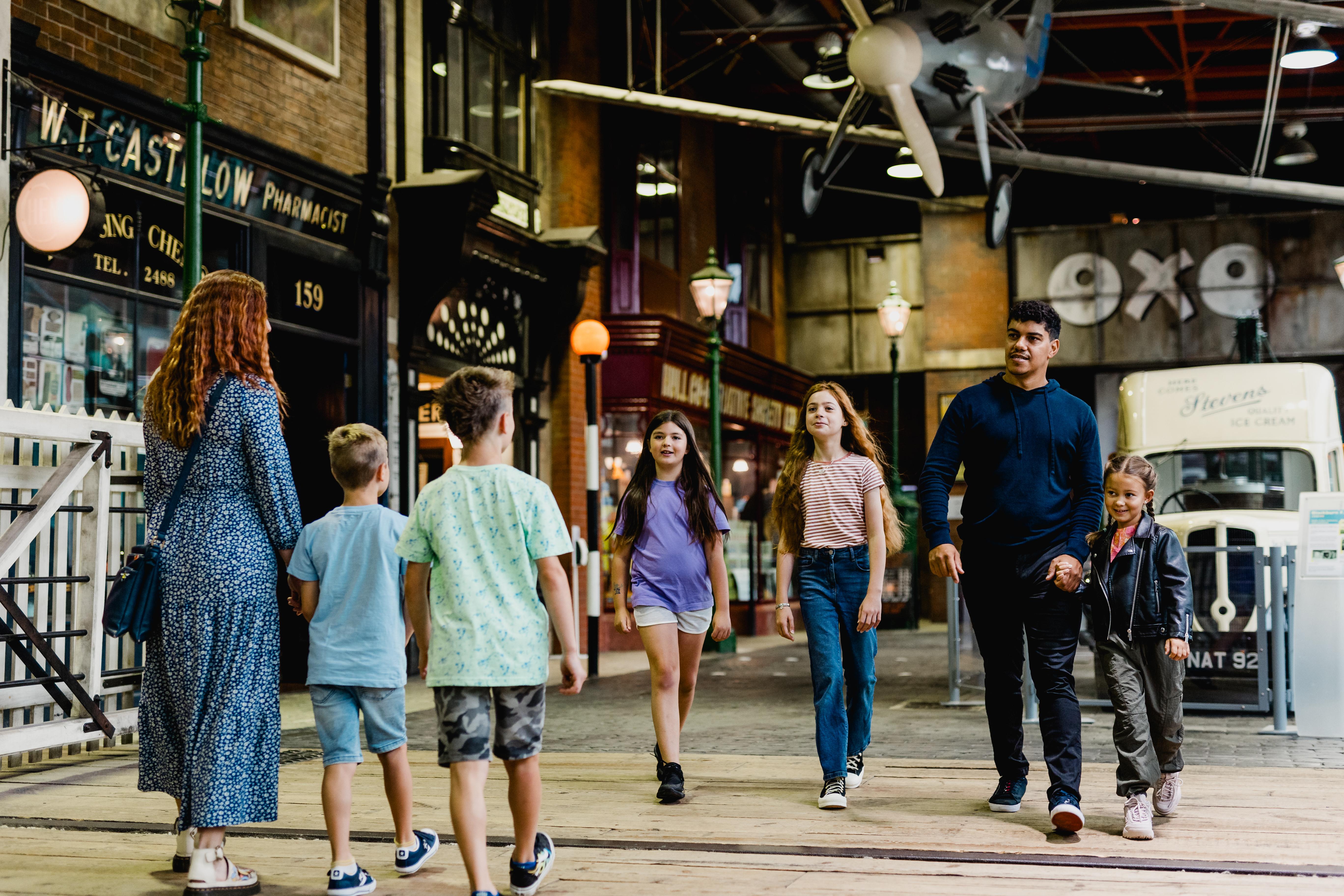 Two families in a museum surrounded by old shops and vehicles.