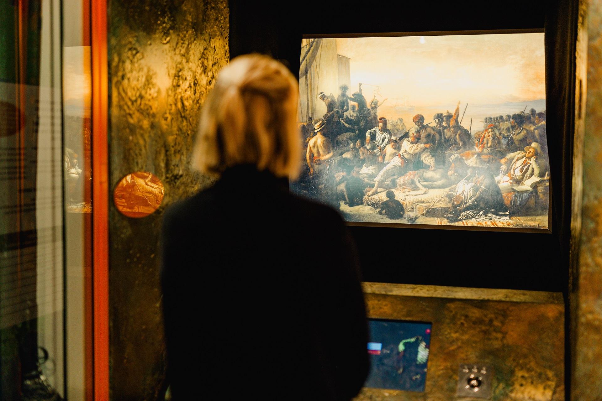 A woman looking at a painting on a screen in a museum.
