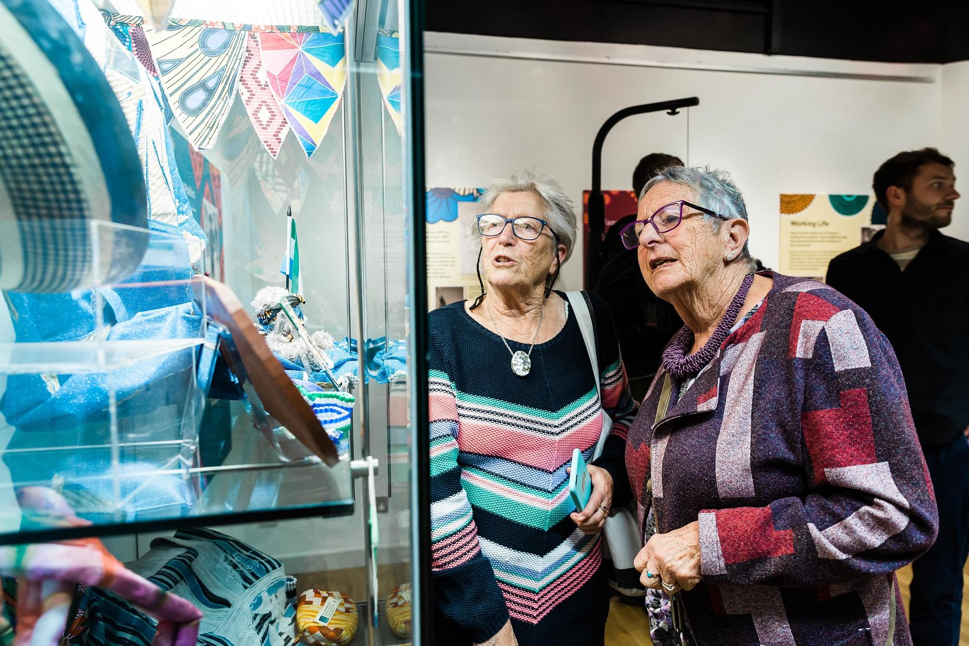Two women looking at objects in a glass display case.