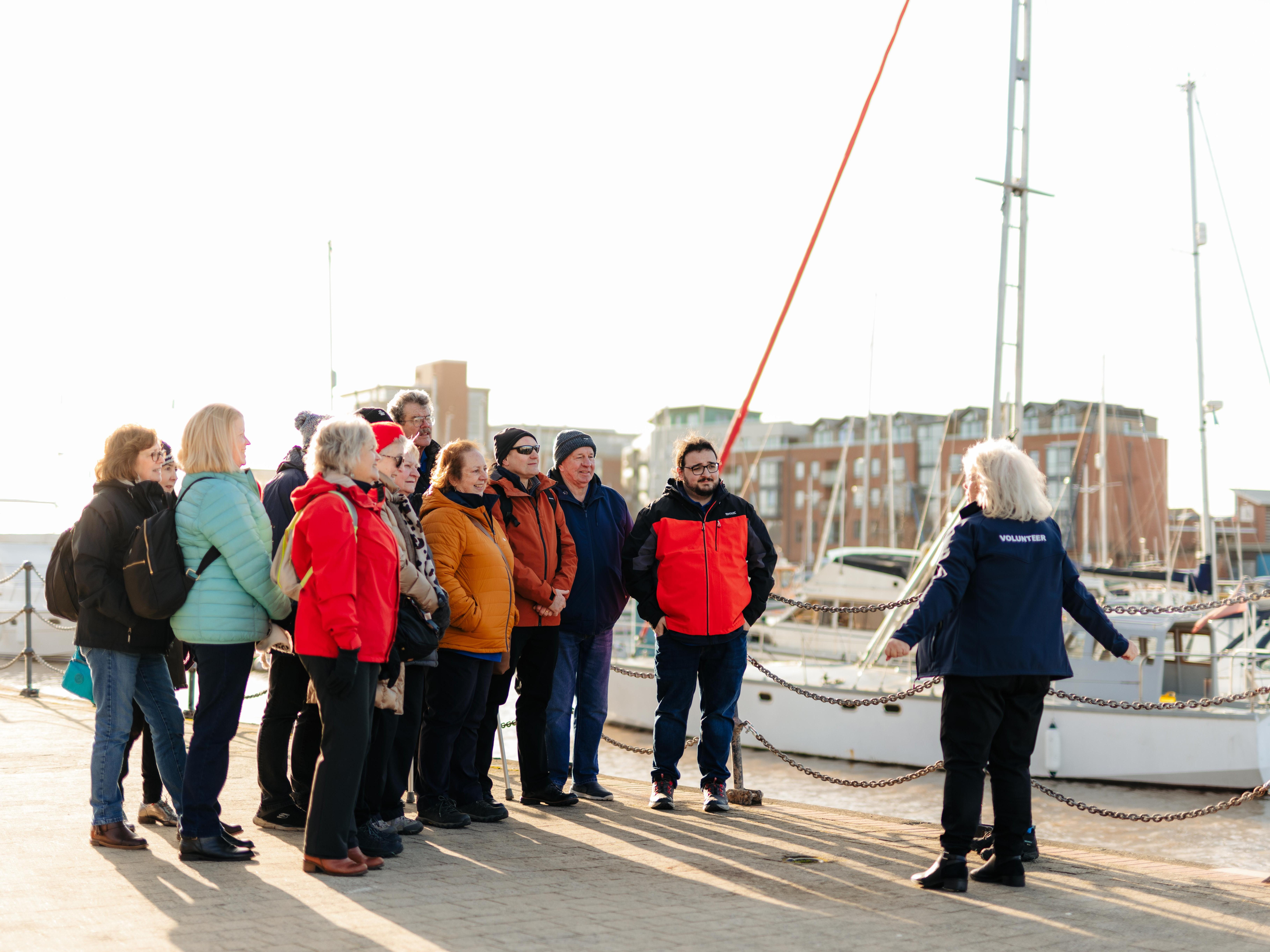 A woman talking to a group of people in front of a boat