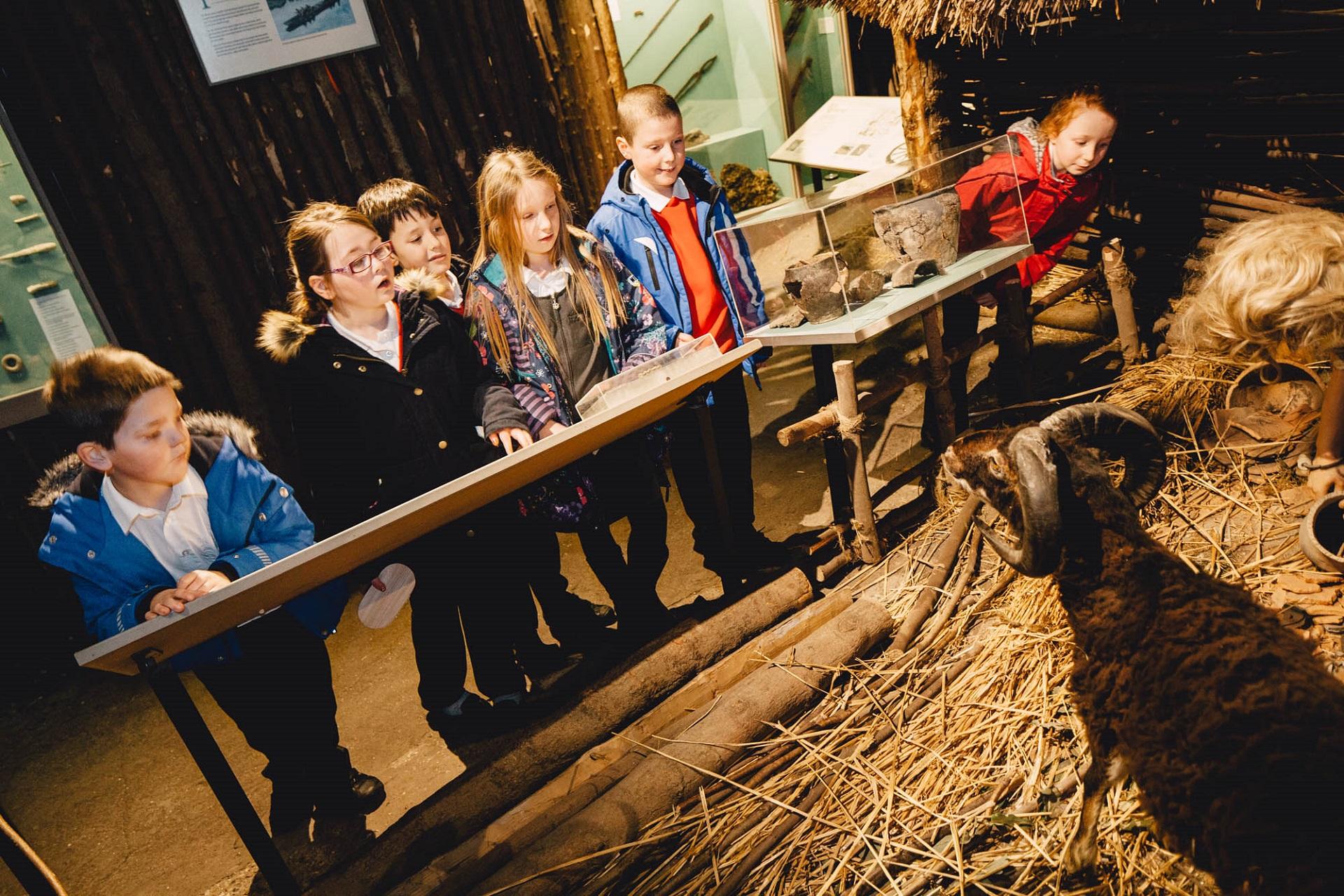 A group of school children looking at a Celtic village display in a museum.