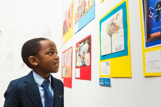 A boy looking at children&#039;s artwork on the wall of a gallery.