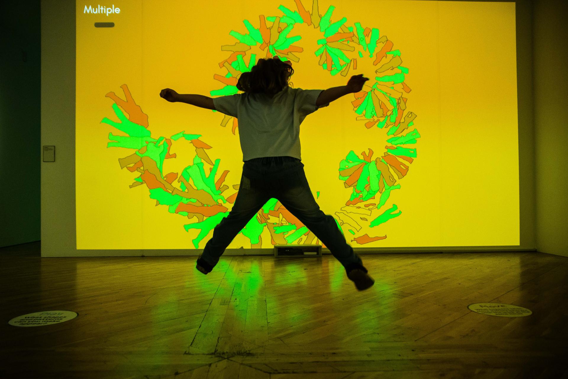 A young girl doing a star jump in front of an illuminated projection