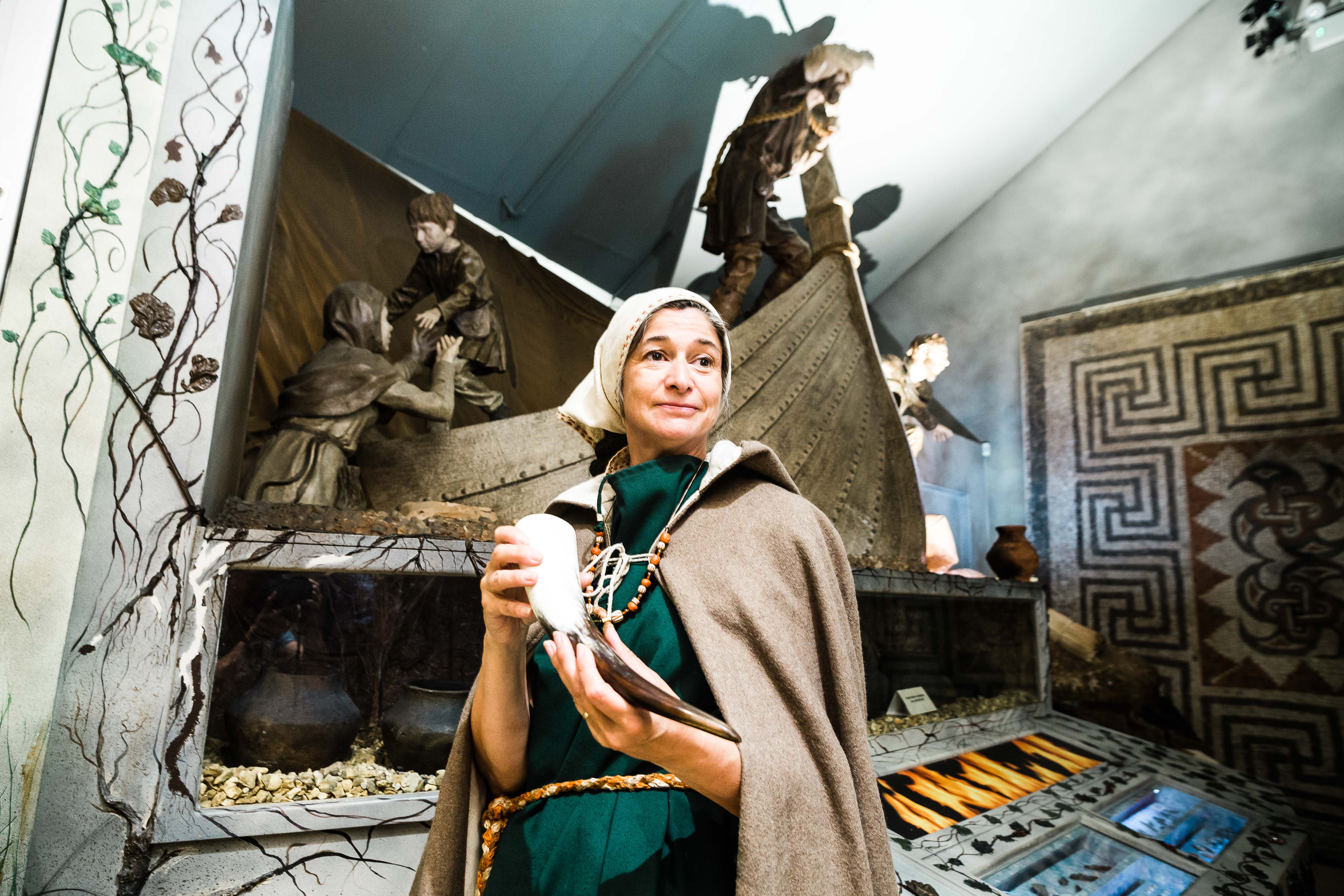 Wulfhilda, an Anglo-Saxon, holding a horned instrument in the Saxon gallery at the Hull and East Riding Museum. Behind her is a Viking longship.