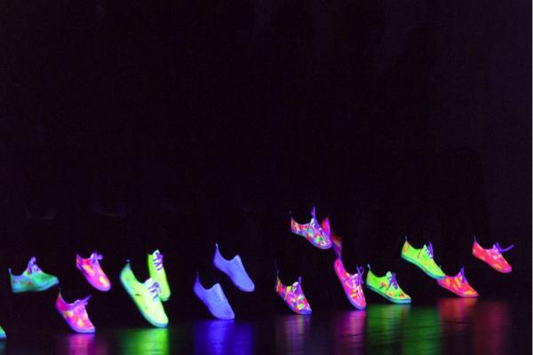 Several pairs of feet wearing brightly coloured shoes set against a dark background