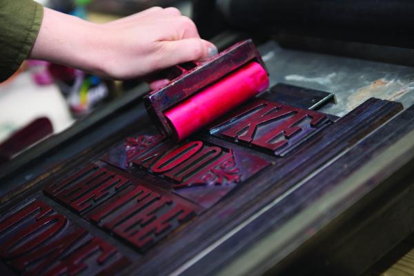 A hand holding a print roller on letter prints