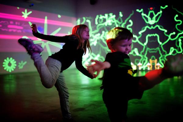 Two children dancing in front of an interactive light display.
