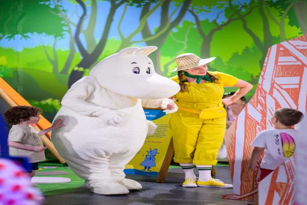Moomin troll stood next to a woman wearing a bright yellow rain suit