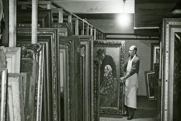 An old photograph of a curator holding a piece of artwork out from the racking in the stores
