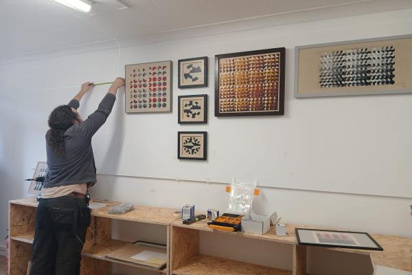 An art gallery technician is measuring a spot on the wall.