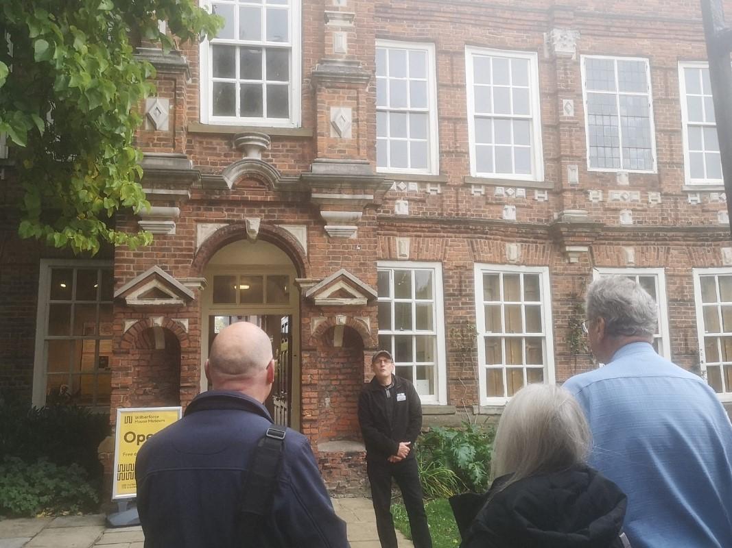 A man in front of a red brick building talking to a group of people.