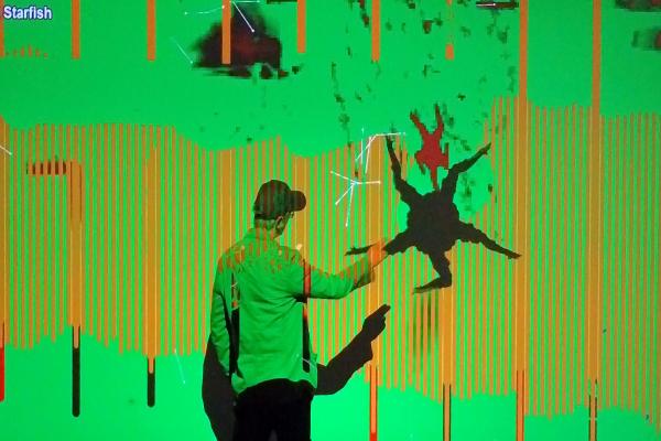 An child interacting with an interactive light display. There is green light shining on him and his shadow is casting.