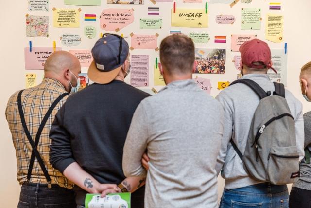 A group of people looking at a display on the wall of an exhibition.