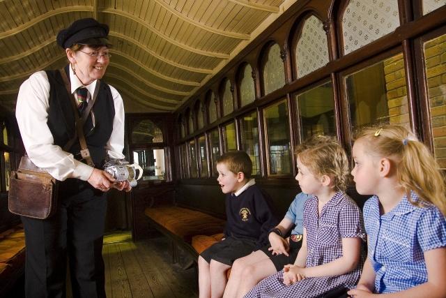 A woman dressed as a tram conductor on a tram with three children.