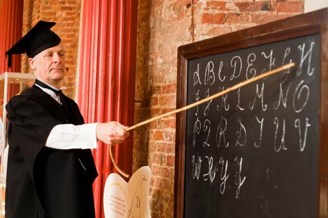 A man dressed as a Victorian era teacher in front of a blackboard