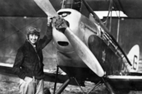 A black and white photo of a pilot stood in front of an aeroplane.