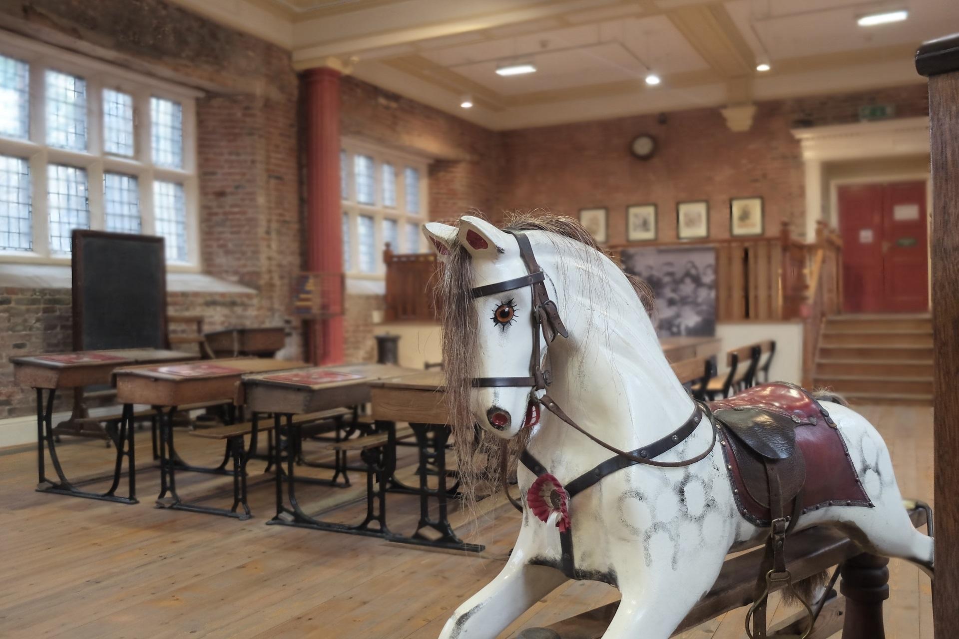 A rocking horse in a Victorian schoolroom setting in a museum.