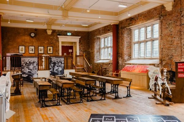 A Victorian schoolroom with wooden desks and chairs in it.